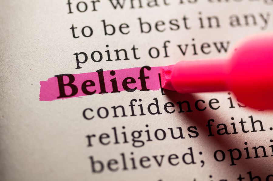 A highlighter pen being used to bighlight the word &quot;Belief&quot; on a printed page