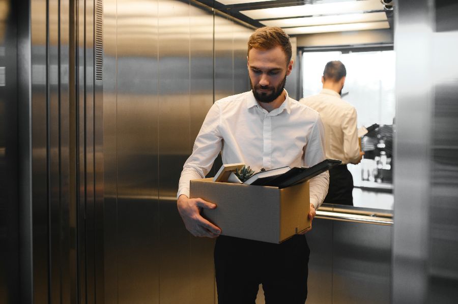 A man carrying a cardboard box away from his workplace