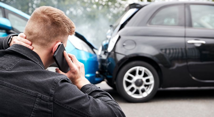 A man using his mobile phone while looking at the result of a crash between two cars